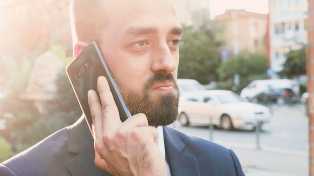 Free photo portrait of businessman in diplomatic suit talking at phone discussing marketing strategy with remote collegue. executive manager standing outside in front of startup building office