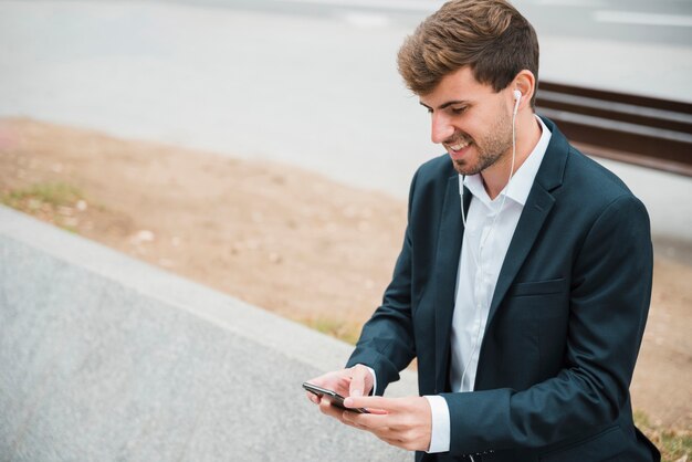 Portrait of a businessman listening music on earphone attached on mobile phone