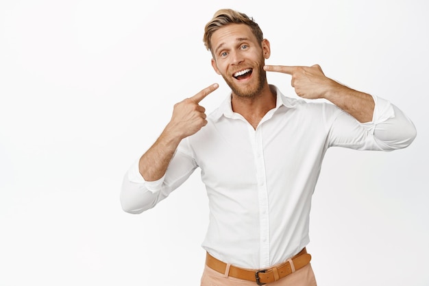 Portrait of businessman pointing at his white teeth perfect whitened smile dental clinic advertisement standing over white background