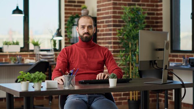 Portrait of businessman sitting at desk and preparing to work on computer to plan financial charts for development. Company employee using e commerce statistics on network app.