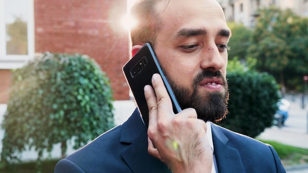 Portrait of businessman talking at smartphone discussing marketing strategy with remote manager explaining company project working at business presentation in front of startup office. Outside concept