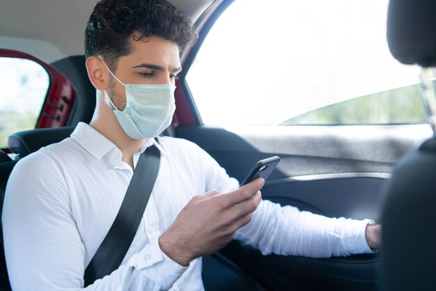 Portrait of businessman wearing face mask and using his mobile phone on way to work in a car