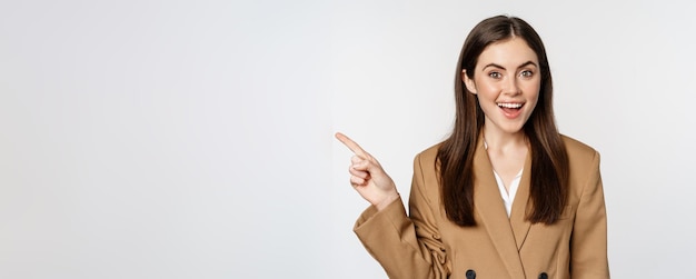 Portrait of businesswoman pointing finger left showing corporate banner logo standing in brown suit