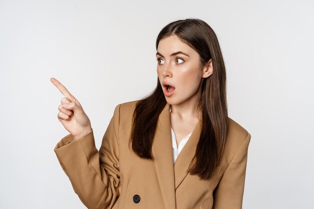 Portrait of businesswoman pointing finger left showing corporate banner logo standing in brown suit ...