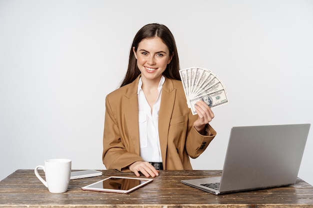 Portrait of businesswoman sitting in office with money working and making profit income posing happy...