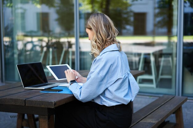 Portrait of businesswoman working on digital tablet checking diagrams sitting outdoors on fresh air