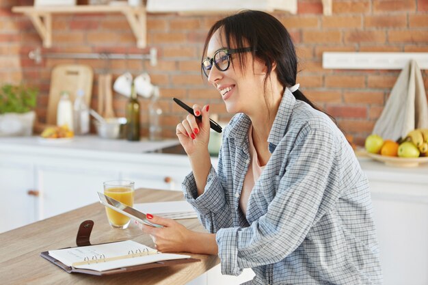 Portrait of busy woman creates project, searches information in tablet, writes notes at notebook