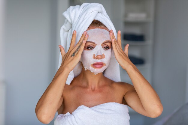 Portrait of calm caucasian pretty woman with a towel on head and a cosmetic mask on face Face skin care concept Female relax on bed at home