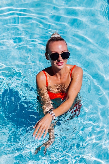 Портрет спокойной счастливой женщины в солнечных очках с загорелой кожей в синем бассейне в солнечный день