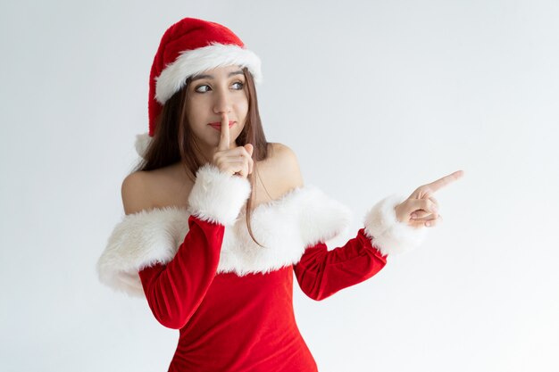 Portrait of calm woman standing with finger on lips and pointing