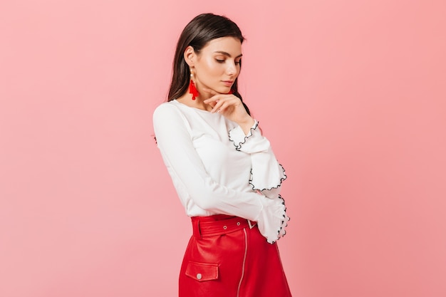 Free photo portrait of calm woman in white blouse and red leather skirt on pink background.