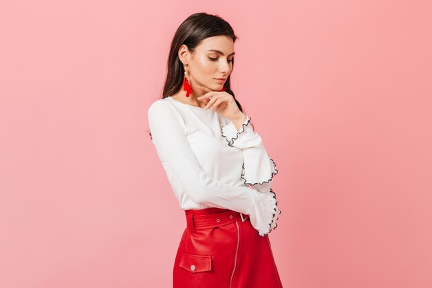 Portrait of calm woman in white blouse and red leather skirt on pink background.