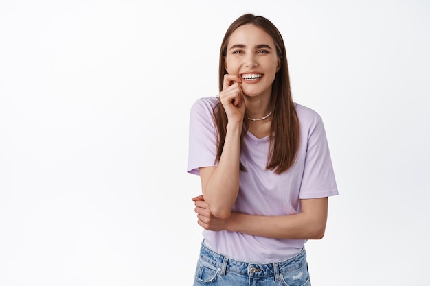 Ritratto di candida donna felice che ride, morde il dito e sorride denti bianchi, guardando la fotocamera spensierata, godendo di una piacevole conversazione vivace, sfondo dello studio.