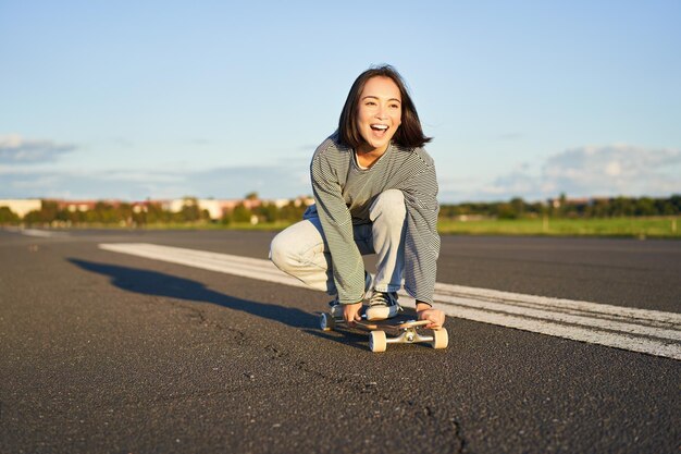 Portrait of carefree happy asian girl skating riding skateboard and laughing enjoying sunny day