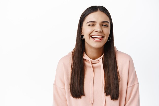 Portrait of carefree young woman winking showing tongue and smiling express happiness positive emotions and joy standing against white background
