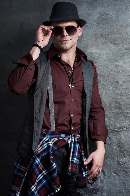 Portrait of casual male dressed in a shirt, waistcoat and sunglasses over grey background.