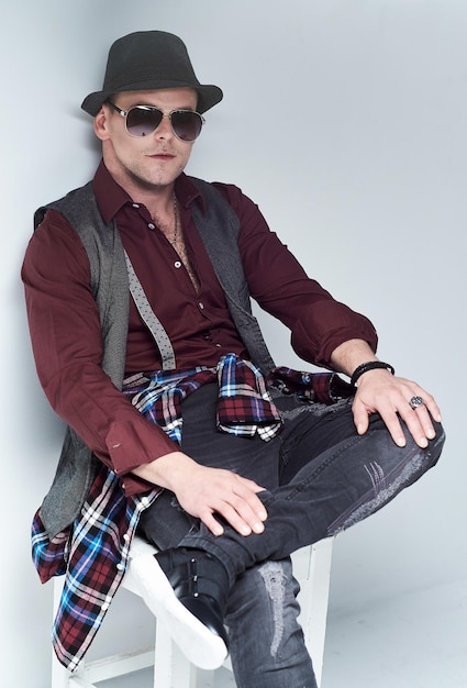 Free photo portrait of casual male dressed in a shirt, waistcoat and sunglasses sits on a chair.