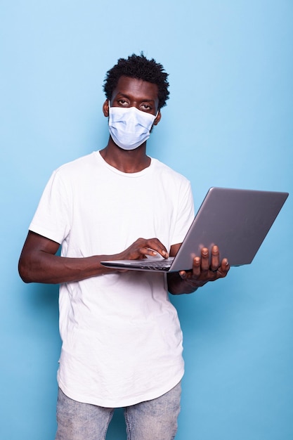 Portrait of casual person holding laptop and wearing face mask