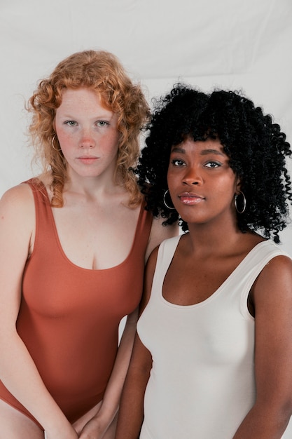 Free photo portrait of caucasian and african young woman looking at camera against grey backdrop