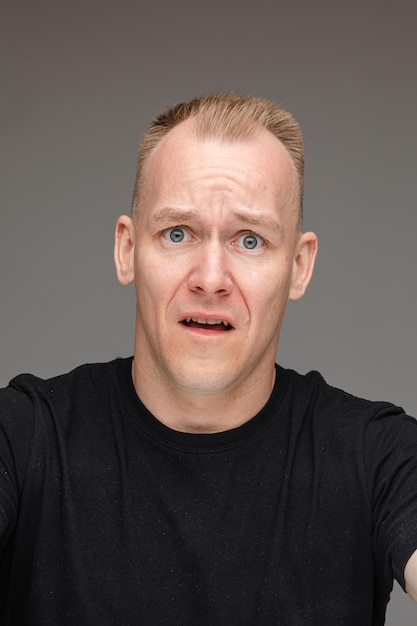 Portrait of caucasian male in black t-shirt looks at something disgust isolated on grey wall