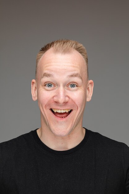 Portrait of caucasian man in black t-shirt and rejoices isolated on grey wall