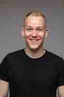 Free photo portrait of caucasian man in black t-shirt and smiles isolated on grey wall