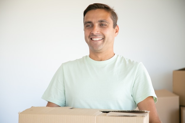 Портрет кавказского мужчины, несущего картонную коробку и улыбающегося
