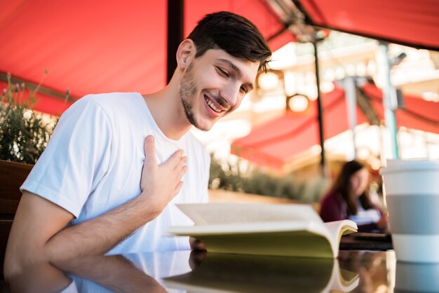 Portrait of caucasian man enjoying free time and reading a book while sitting outdoors at coffee shop. Lifestyle concept.