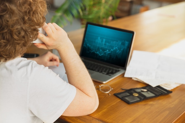 Portrait of caucasian unset and despair man watching financial and economical graphs during coronavirus quarantine, problems