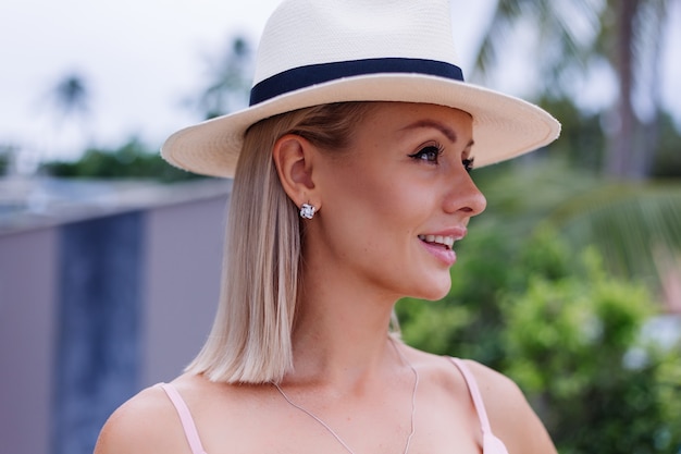 Portrait of caucasian woman in romantic elegant pink long dress on vacation at luxury rich villa hotel with amazing tropical palm trees view Female in classic white hat