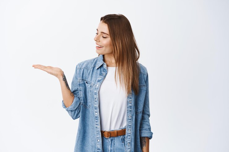 Free Photo portrait of caucasian young woman holding product on palm, looking at empty hand as if having something in it, smiling pleased, standing on white