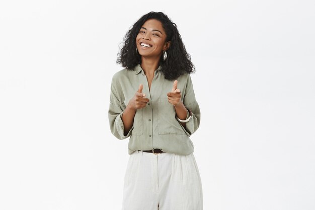 Portrait of charismatic friendly and upbeat attractive dark-skinned young female in blouse and pants pointing with fingers