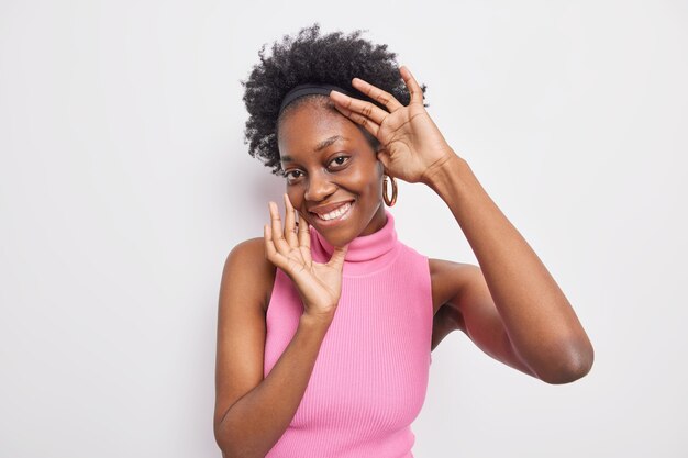 Portrait of charming African American woman touches face gently smiles broadly has white teeth 