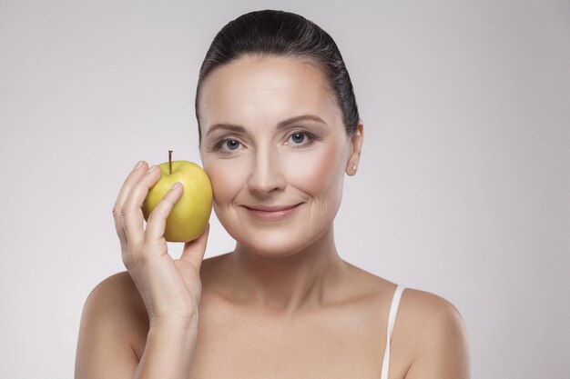Portrait of charming beautiful healthy caucasian middle aged woman holding green apple, she love to eat fruit, make her get good health, nice skin, lose weight and weight control. copy space, indoor