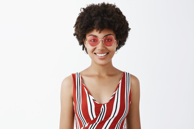 Портрет очаровательной беззаботной и милой афроамериканки в солнечных очках и модной полосатой одежде, радостно улыбаясь