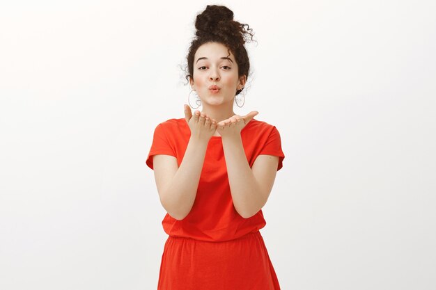 Portrait of charming caring european female with curly hair combed in bun wearing cute red dress