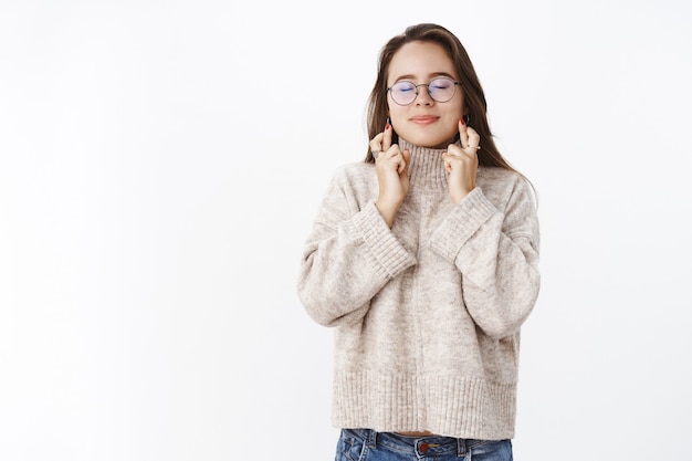 Portrait of charming dreamy girl making wish with crossed fingers for good luck and closed eyes