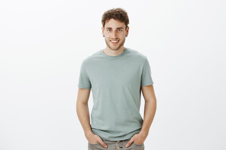 Free Photo portrait of charming flirty aduly guy with blond hair, holding hands on pants and smiling broadly, talking with friends casually while hanging out and relaxing