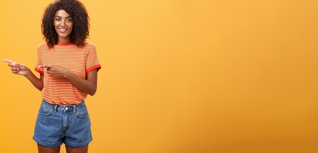 Portrait of charming friendlylooking africanamerican female coworker in casual outfit pointing left