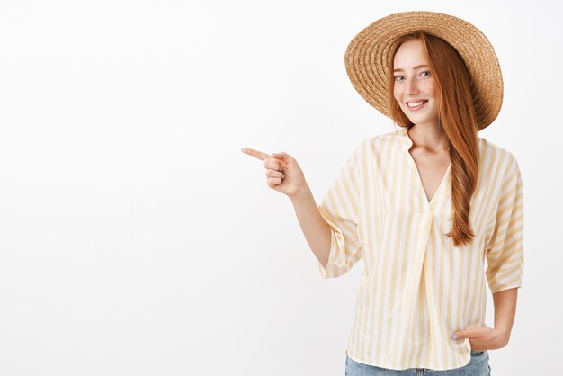 麦わら帽子とトレンディな黄色のブラウスを左のビーチで夏の日を楽しんでいる魅力的な幸せとフェミニンな赤毛のスタイリッシュな女性の肖像画