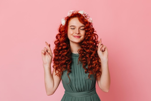 Free photo portrait of charming lady in khaki dress smiling and crossing her fingers girl with red curly hair smiles with closed eyes