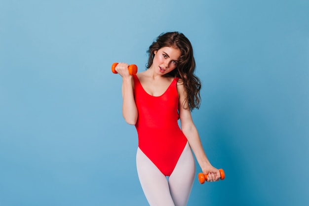 Портрет очаровательной спортивной женщины в красном купальнике и леггинсах, делающей упражнение на бицепс
