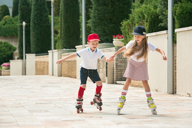 Portrait of a charming teenage couple skating together on roller skates at park. Teen caucasian boy and girl. Children colorful clothes, lifestyle, trendy colors concepts.