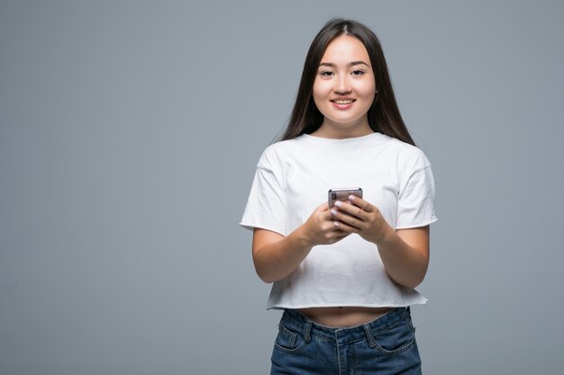 携帯電話を押しながら灰色の背景の上にカメラを見て陽気なアジアの女性の肖像画