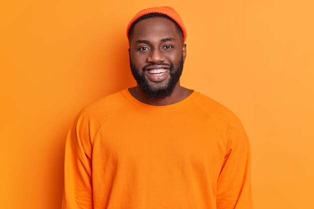 Portrait of cheerful bearded African American man has happy expression smiles broadly has white perfect teeth