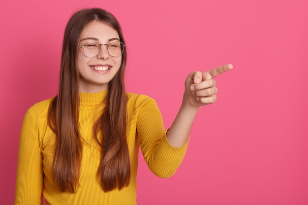 Portrait of cheerful beautiful female ridiculing, laughing at somebody, making gesture, pointing at something with forefinger