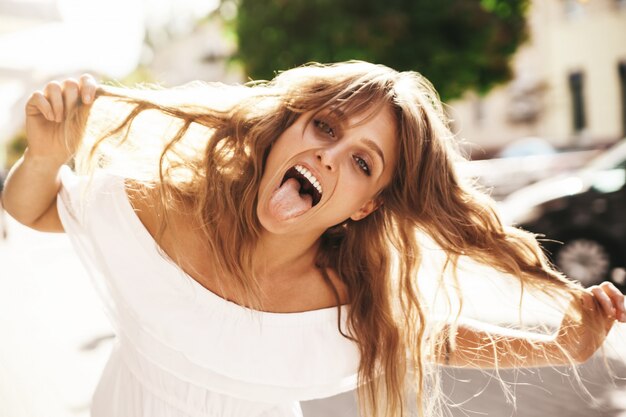 Portrait of cheerful blonde hipster girl without makeup  going crazy making funny face and showing her tongue on the street background. Touching her hair