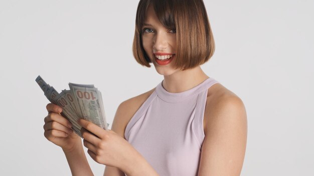 Portrait of cheerful brunette girl happily counting money on camera over white background. Carefree girl