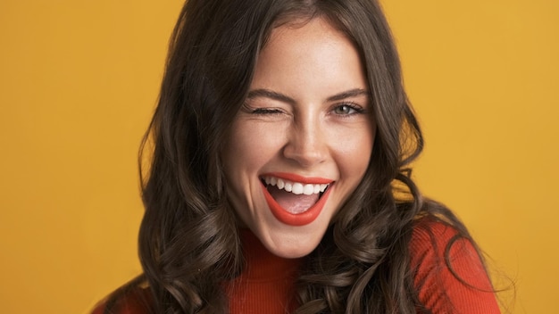 Free photo portrait of cheerful brunette girl with red lips joyfully winking on camera over colorful background