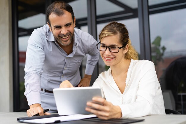 Portrait of cheerful colleagues discussing documents on tablet